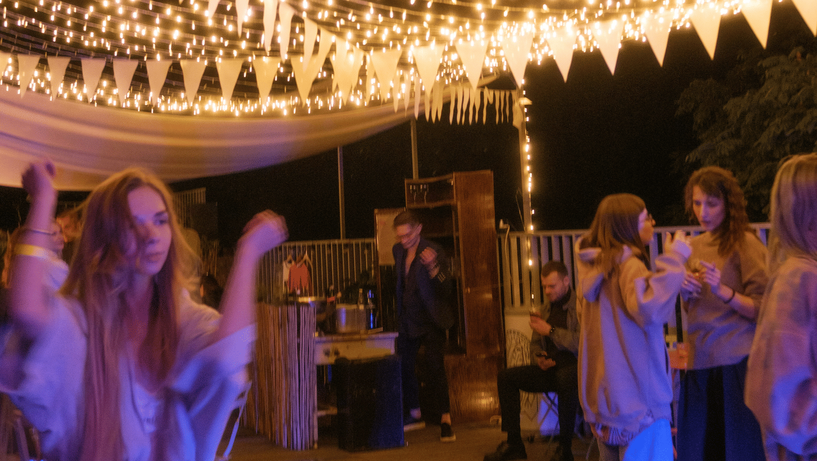 A view of a rooftop party on a hotel near Sukhumvit Soi 11, with lights hung above and people dancing and talking to each other.