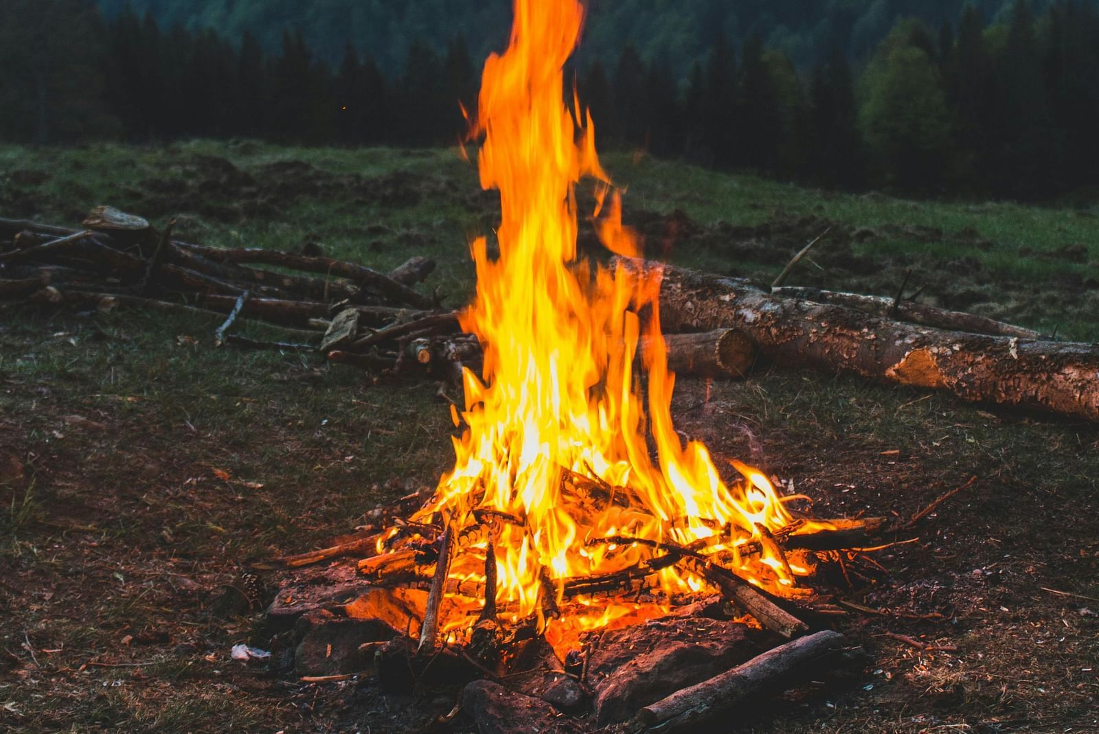 A campfire burns brightly in a mountain landscape at dusk.