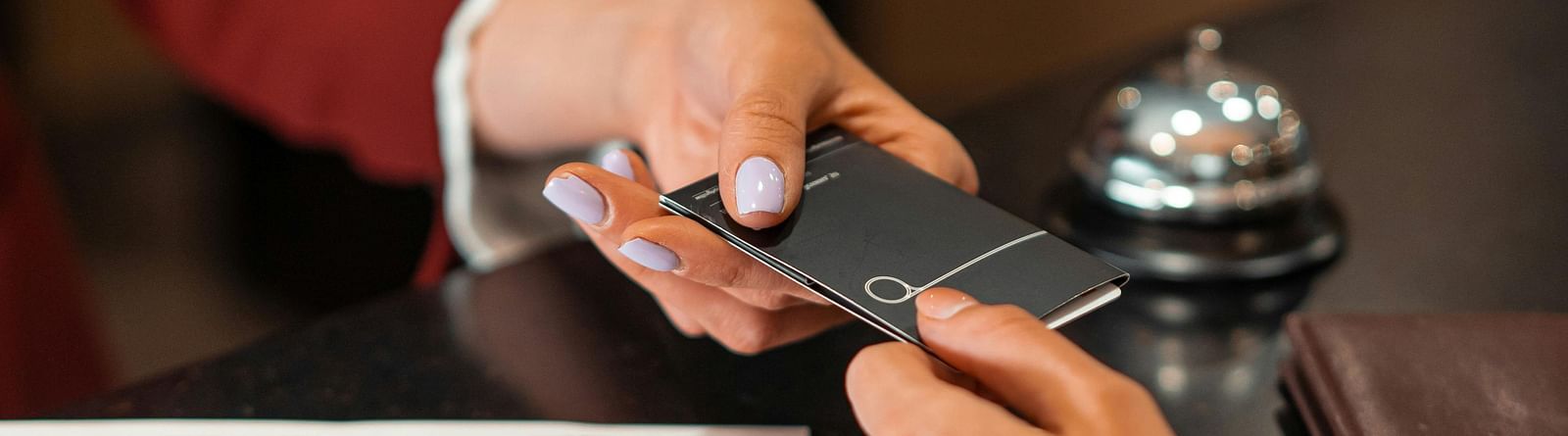A hand holding out a card over the reception desk, with another hand gripping the other end.