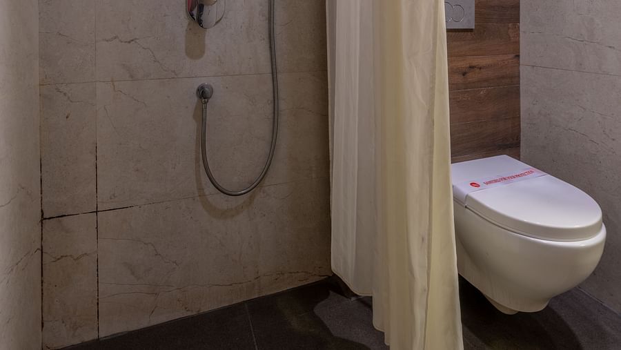 A shower area with handheld shower and a toilet in a tiled bathroom at Hotel Highway King, Jaipur.