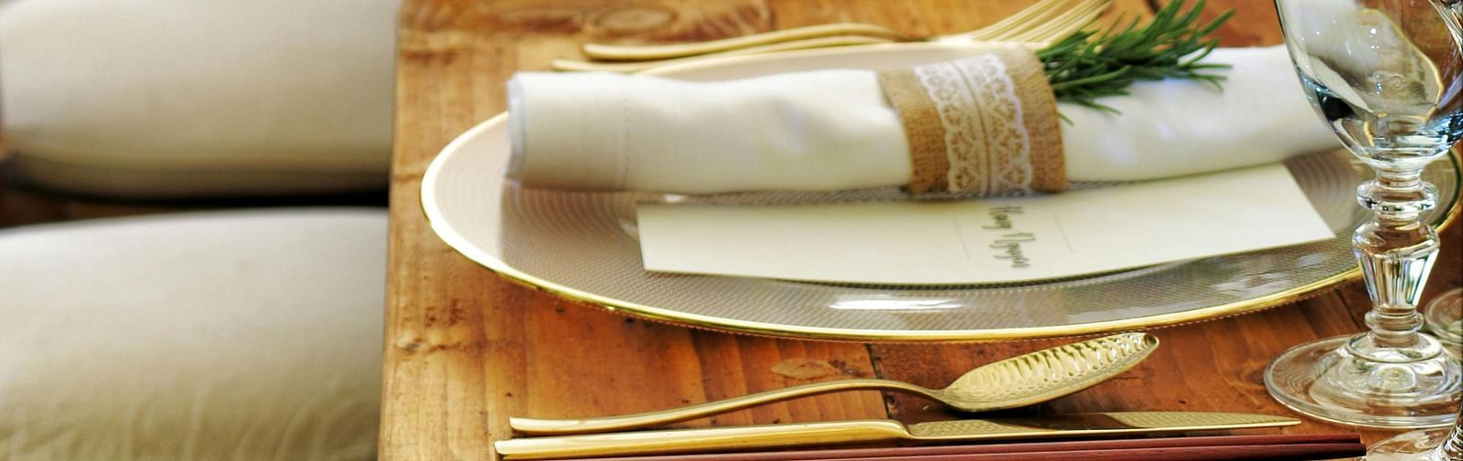 a long wooden table with beautifully set cutlery with small fern leaves in vases