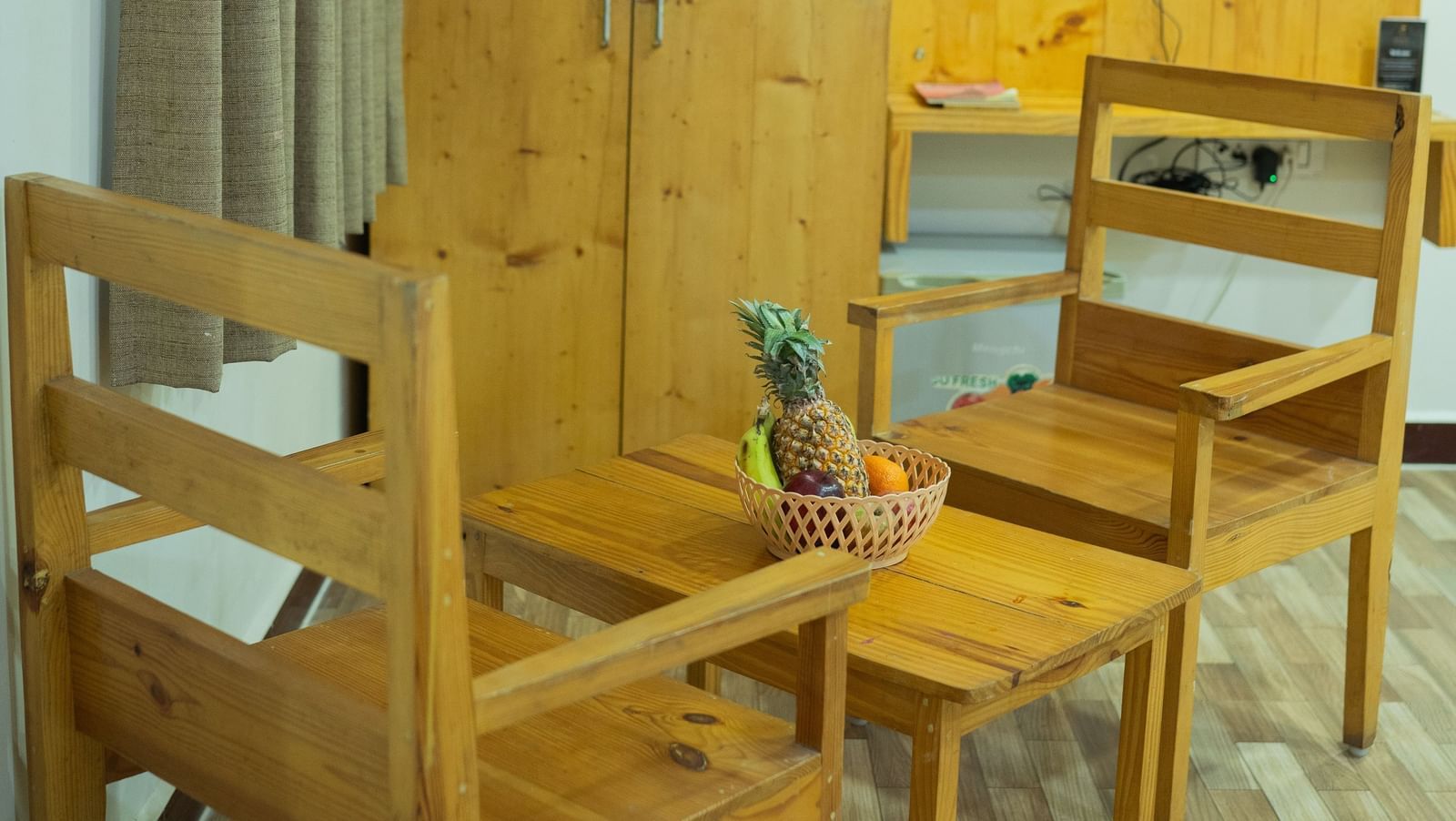 A small dining space with wooden chairs, wardrobe, and T.V., in a guest room at Daksh Resort & Amusement Park, Sasan Gir.