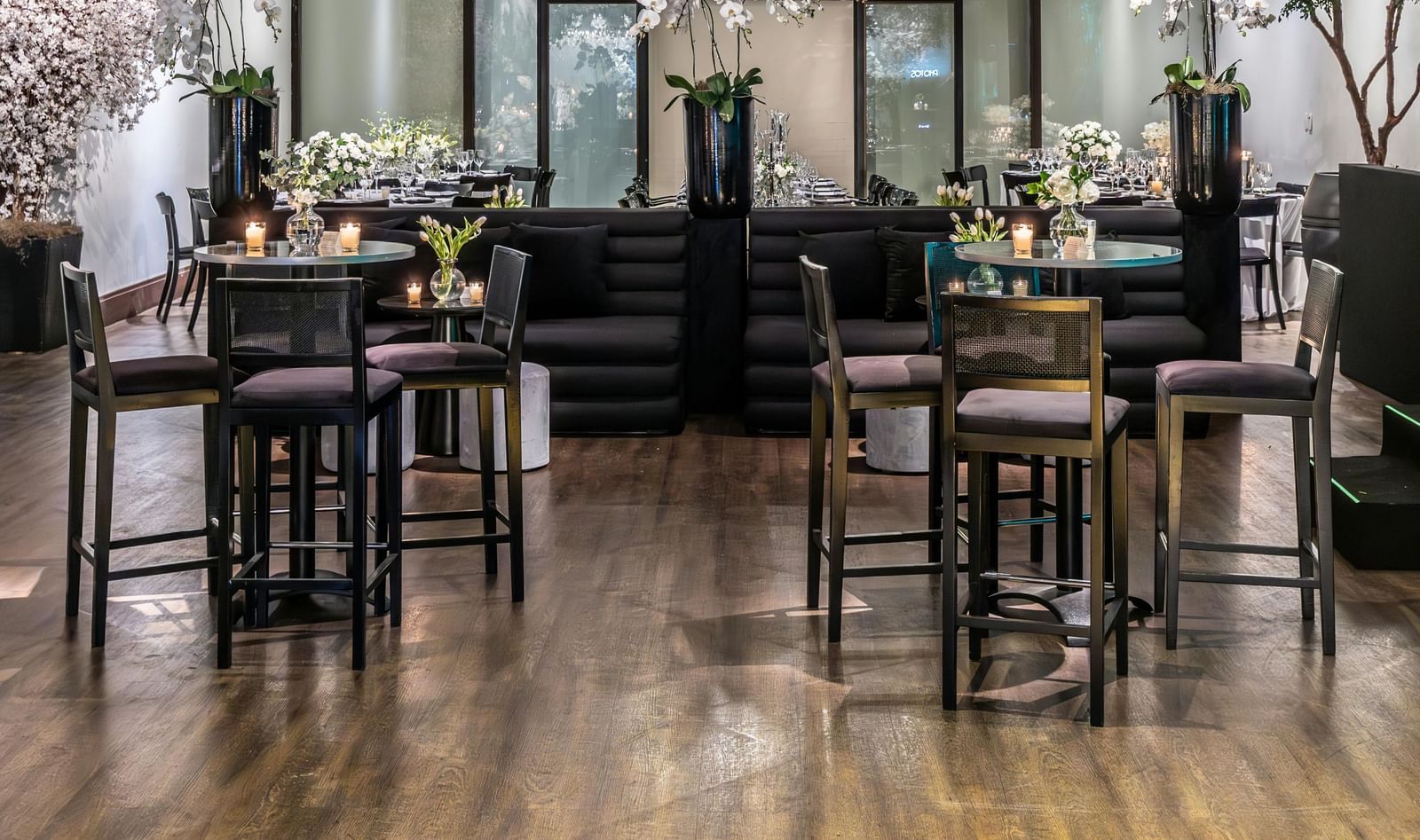 Brightly lit indoor event space with small tables, chairs, and floral decorations.