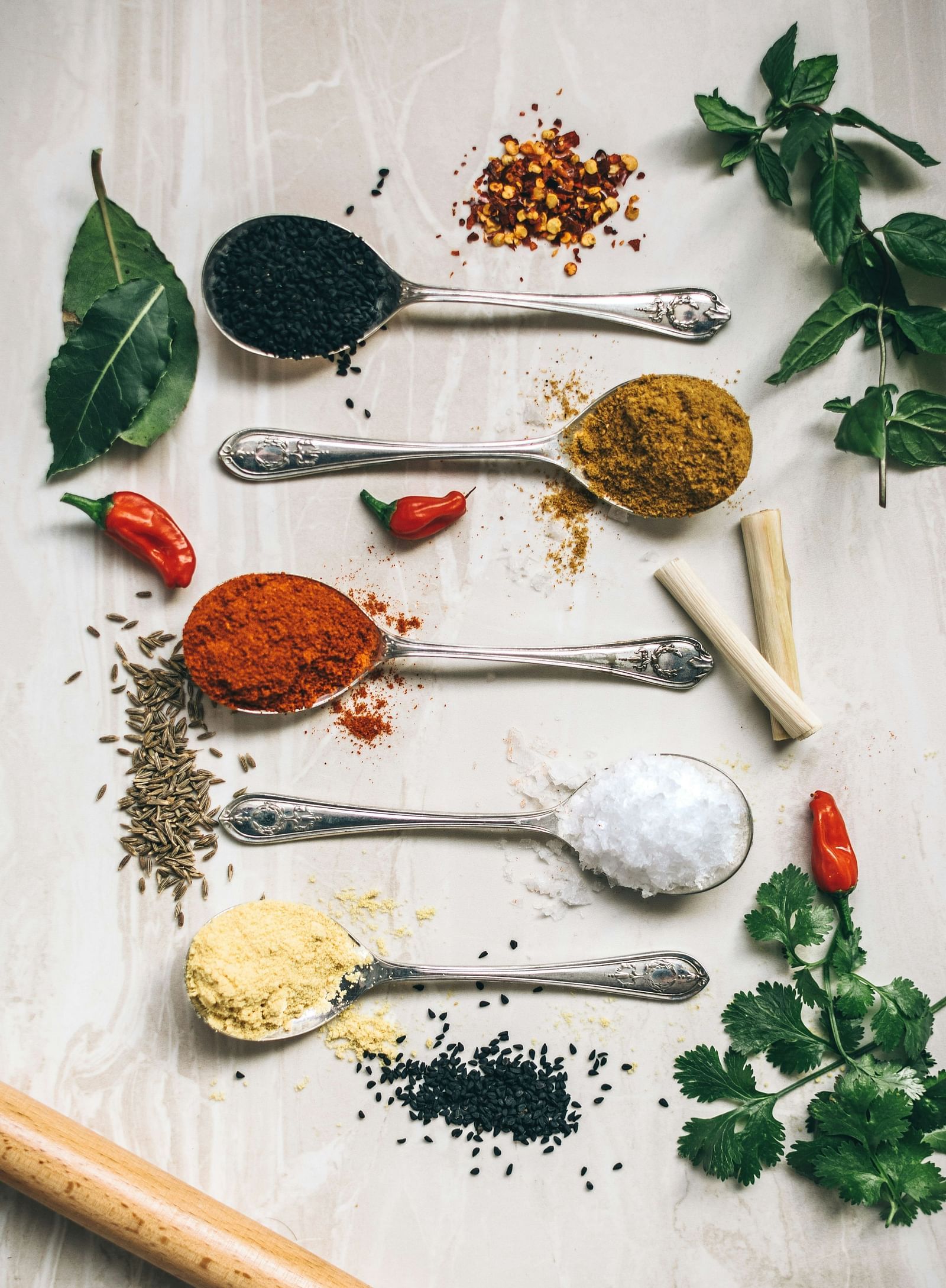 an image showing many spoons with different spices on it and leaves next to it