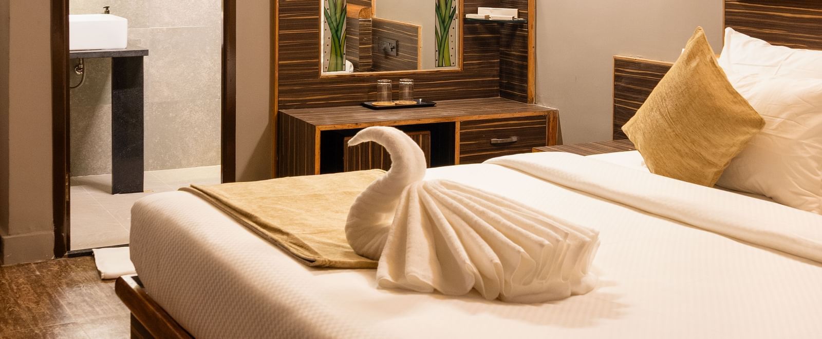 A cosy bedroom features a neatly made bed with white linens and pillows, a mirror reflecting part of the room, and warm lighting | Standard Room | RD's Nature Retreat, Bangalore