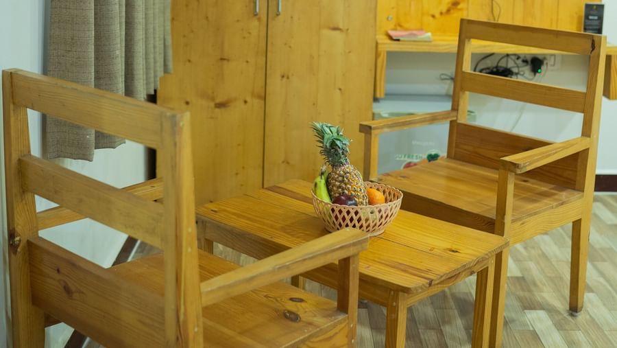 A close-up view of seating area with wooden chairs & a table with a wooden wardrobe and a wall mounted TV at the background at Daksh Resort & Amusement Park, Sasan Gir.