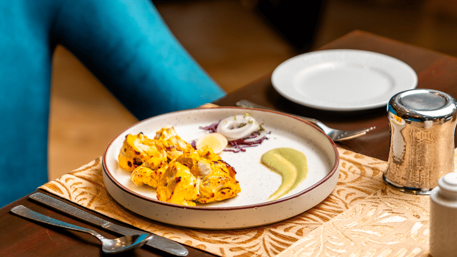 A close-up of a table setting at Za-aiqa, showing a plate of freshly prepared appetizers served with green chutney and sliced onions on a patterned cream table runner.