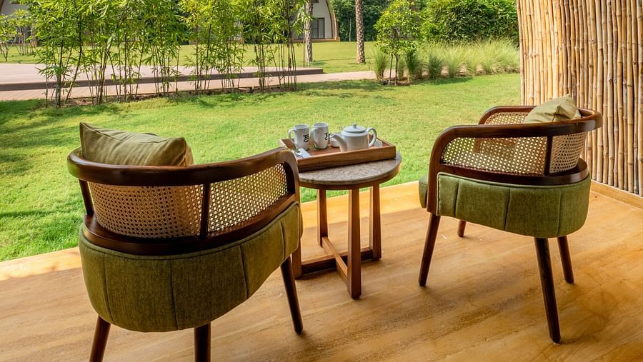 An image of two chairs with tea table placed in a balcony from where villas can be seen