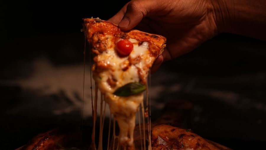 Tasteful close up of a slice of a pizza pulled out by a hand featuring loaded veggies and cheese at Rangamati Garden Resort.