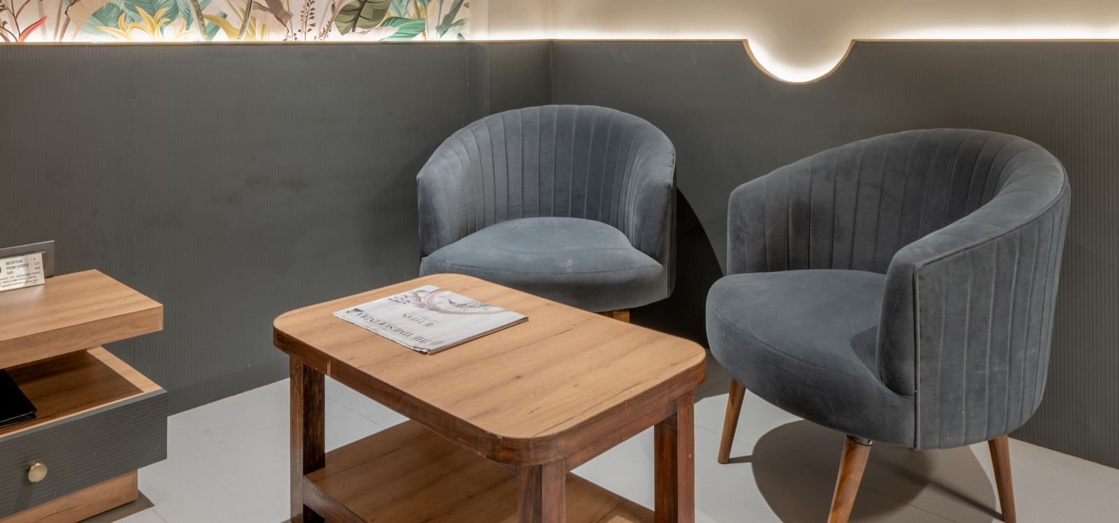 A seating area with two grey chairs and wooden table beside a wall mural at Hotel Highway King, Jaipur.