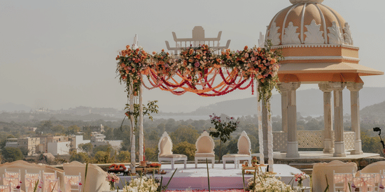 A wedding set up featuring a decorated canopy and a small architectural structural surrounded by plans and flowers.
