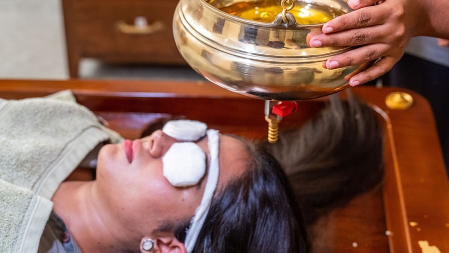 A woman receiving Shirodhara treatment at our wellness centre from a masseuse   - Rajbagh Wellness, Udaipur