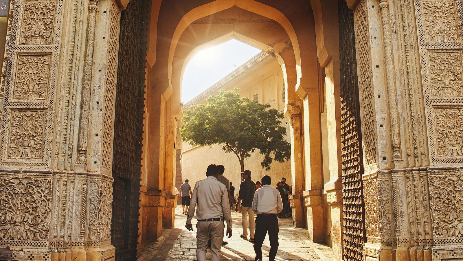 image of a palace entrance with a few people walking into it featuring bright golden sunlight in the other side of the entrance