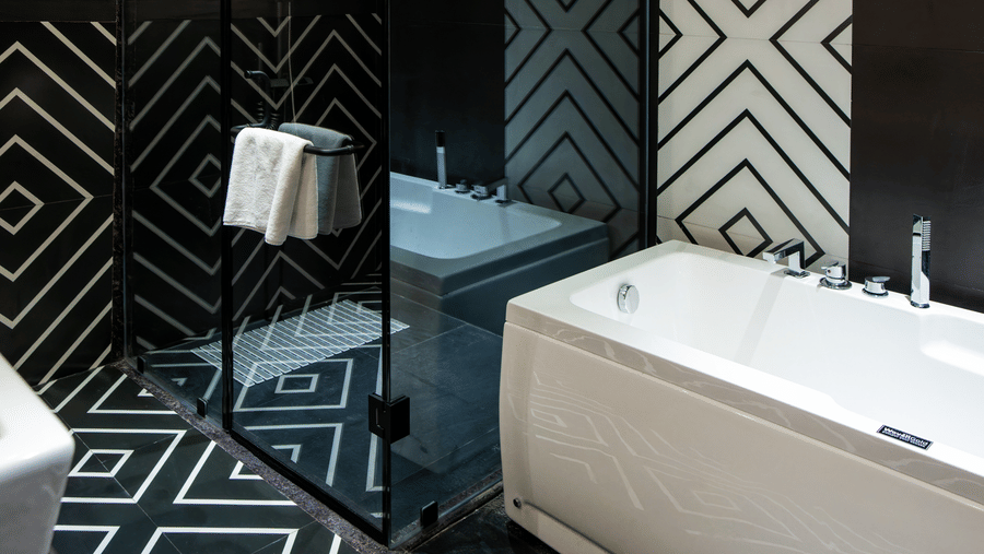 Our Suite bathroom featuring a bathtub, rain shower setup, black-and-white patterned flooring, and modern vanity fittings | Hotel Sonar Bangla, Susunia