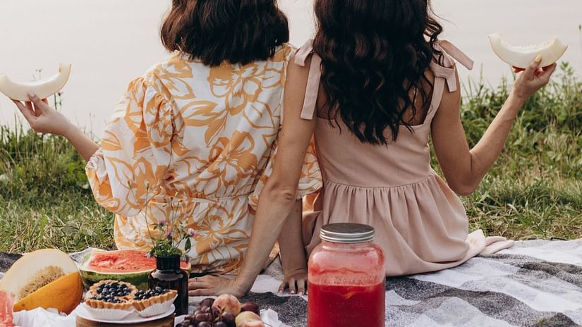 Two women sitting on a blanket next to a body of water