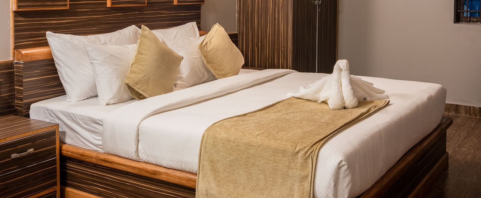 A comfortable bedroom is furnished with a large bed featuring a wooden headboard, soft lighting, and a view of the room's interior | Standard Room | RD's Nature Retreat, Bangalore
