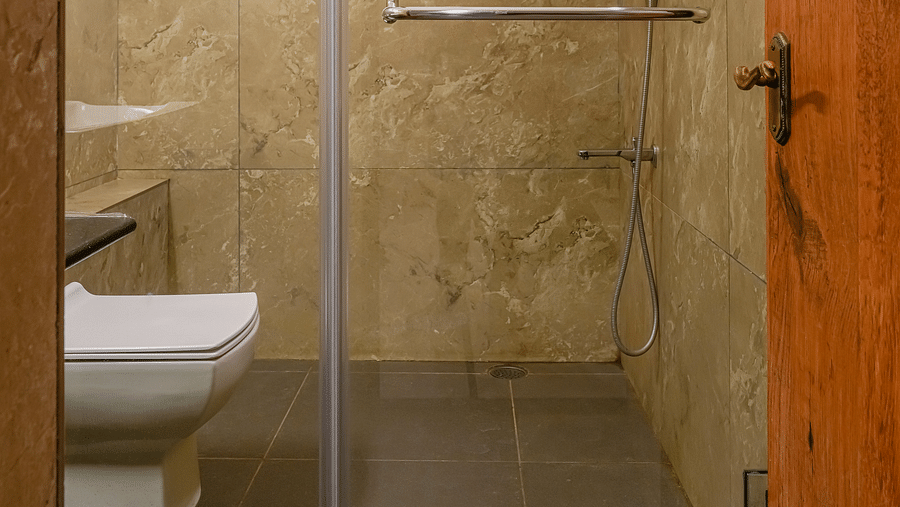 An image of a modern bathroom with a shower head, a commode, and tiled floor - Cross Roads Inn, Bengaluru