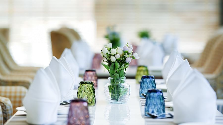 A view of a table featuring neatly arranged napkins, glasses, and cutlery, with flower vases placed in between - NAMAMI BY ZENQ BANKHANDI