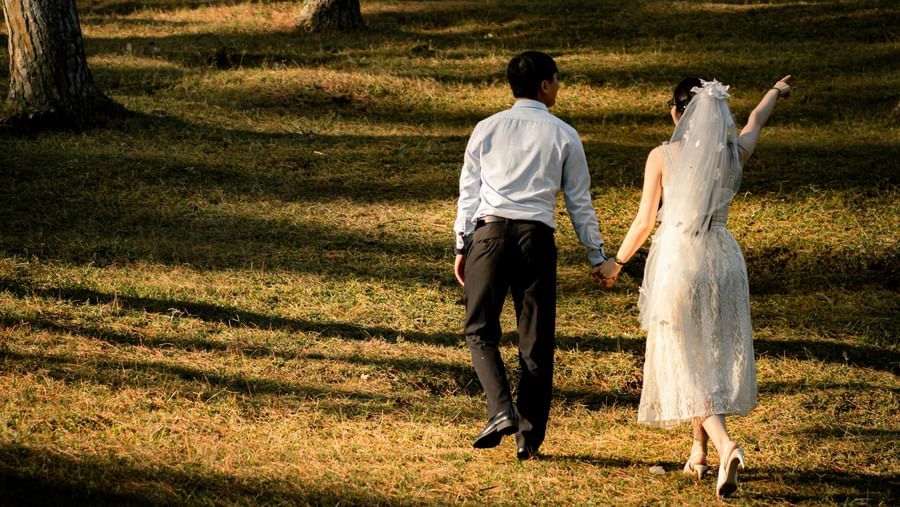 A newly married couple walks hand-in-hand through a sunlit forest, a beautiful setting near the Tallman Hotel.