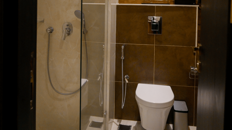 A modern bathroom highlighting a glass shower enclosure next to a wall-mounted toilet and a textured brown wall feature at Tiara by MPS.