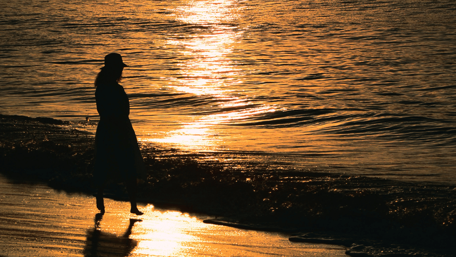 A silhouette of a person standing on a beach, looking out at the sea during a vibrant orange sunset.