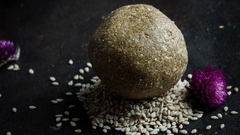 a laddu placed on a plate with sesame seeds below it and flowers next to it