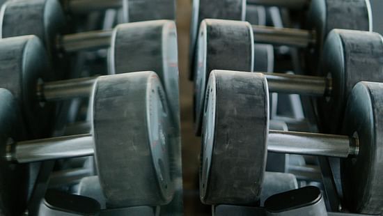 Rows of dumbbells neatly arranged on racks, reflected in a mirror, creating a symmetrical pattern in a gym setting.