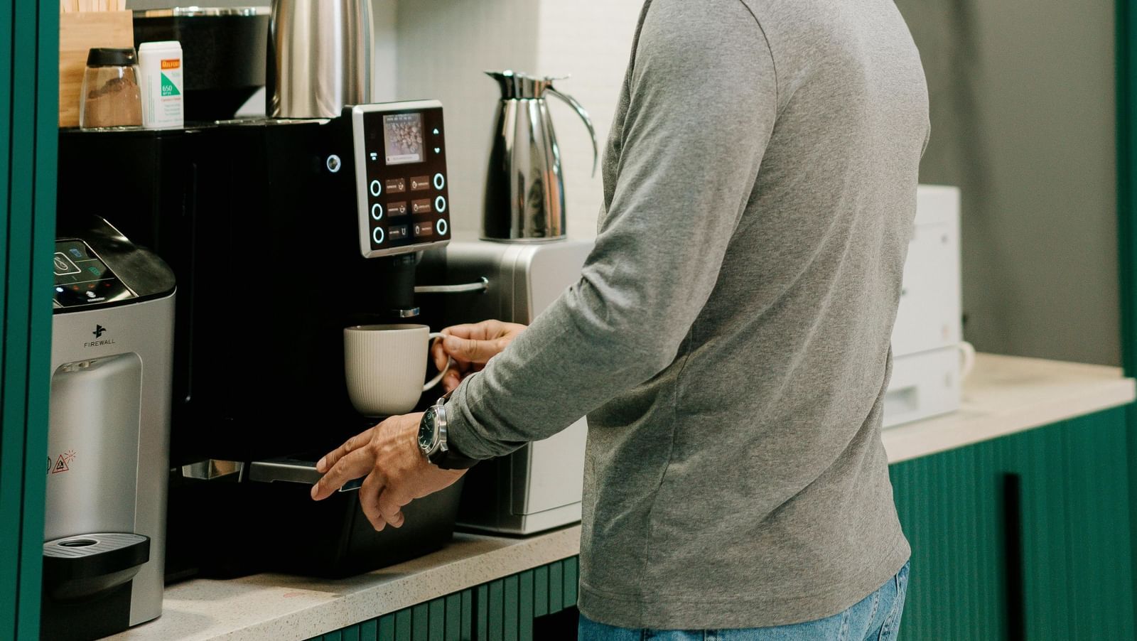 A man getting  cup of coffee at a well-lit coffee station