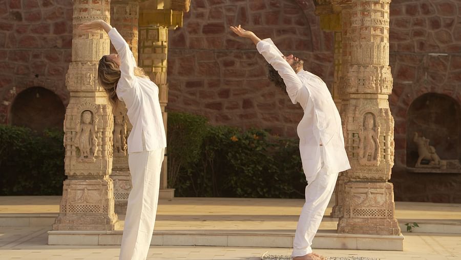 Two people stretching with a baradari in the background at Surpura Bagh.