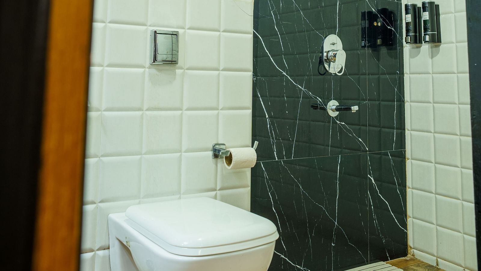 A modern bathroom at Orsino Spa Resort with a toilet and a shower cubicle with dark-coloured tiling.
