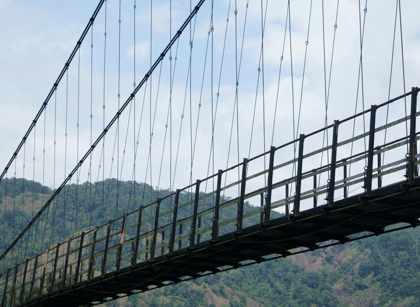 A close-up of the cables and railing of a suspension bridge against a blue sky