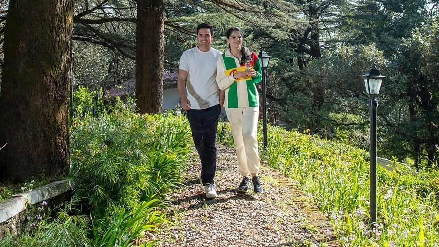 a couple walking through a green garden with huge trees