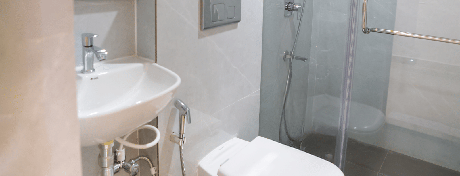 A small bathroom with a toilet, a shower area, and a sink basin at Sunrise Business Hotel, Hyderabad.