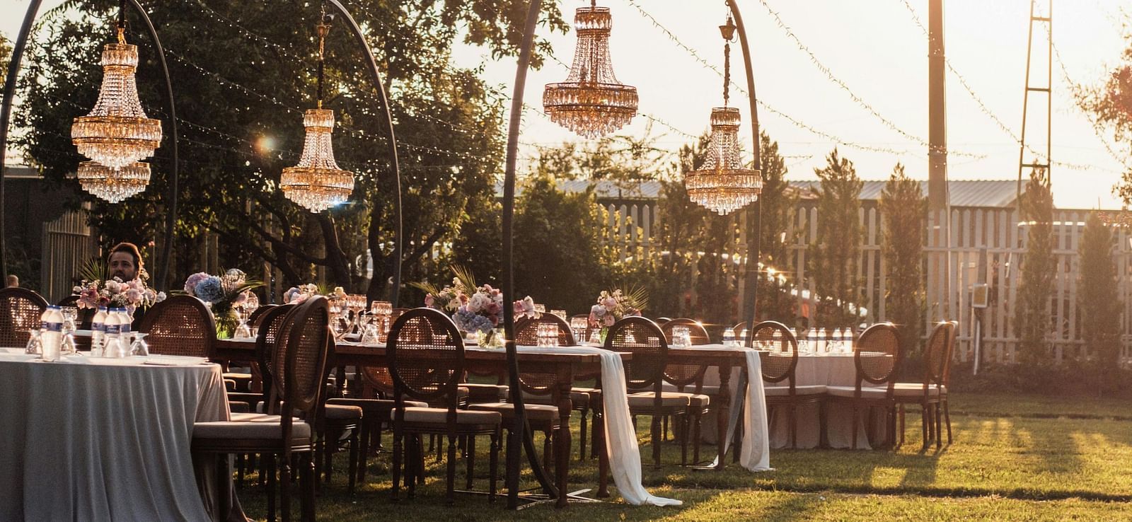 A beautiful lawn area with tall poles holding the decorative strings with a bright sun setting in the background.