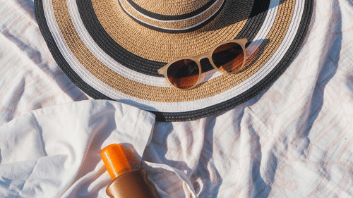 A Hat, Sunglasses and Sunscreen on a Blanket on the Beach