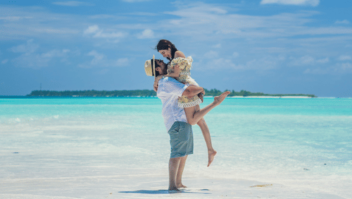 Barefoot At Havelock - image of a couple embracing each other while standing on white sand with the ocean in the background