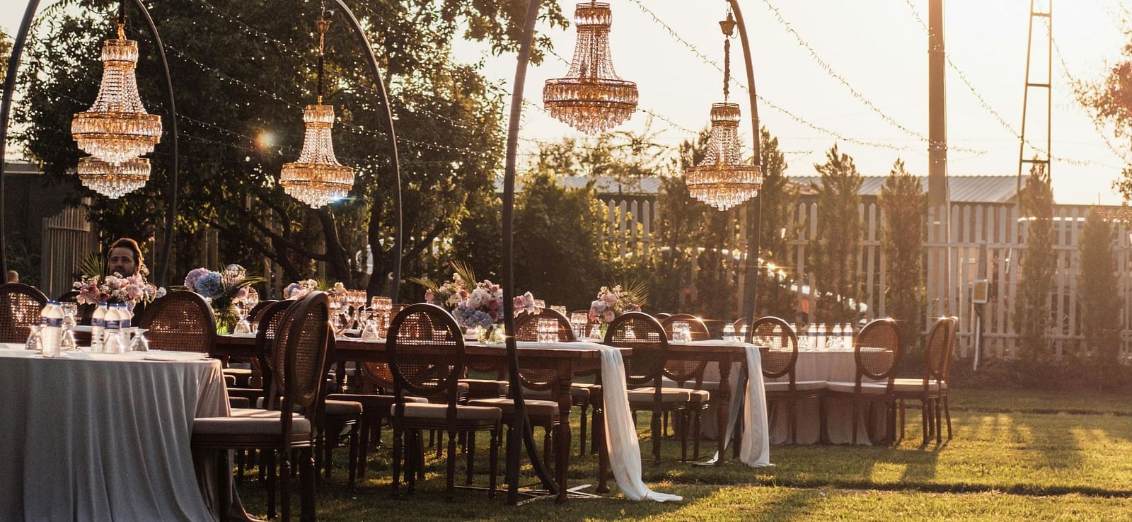 A beautiful lawn area with tall poles holding the decorative strings with a bright sun setting in the background.