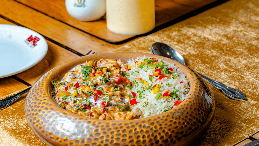 A baked dish in a rustic bowl at Marble Arch, part of the Noor-Us-Sabah Palace, Bhopal, served on a table with a floral centerpiece and candlelight.