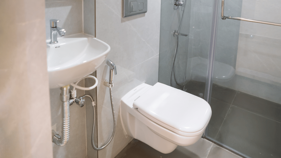 A small bathroom with a toilet, a shower area, and a sink basin at Sunrise Business Hotel, Hyderabad.