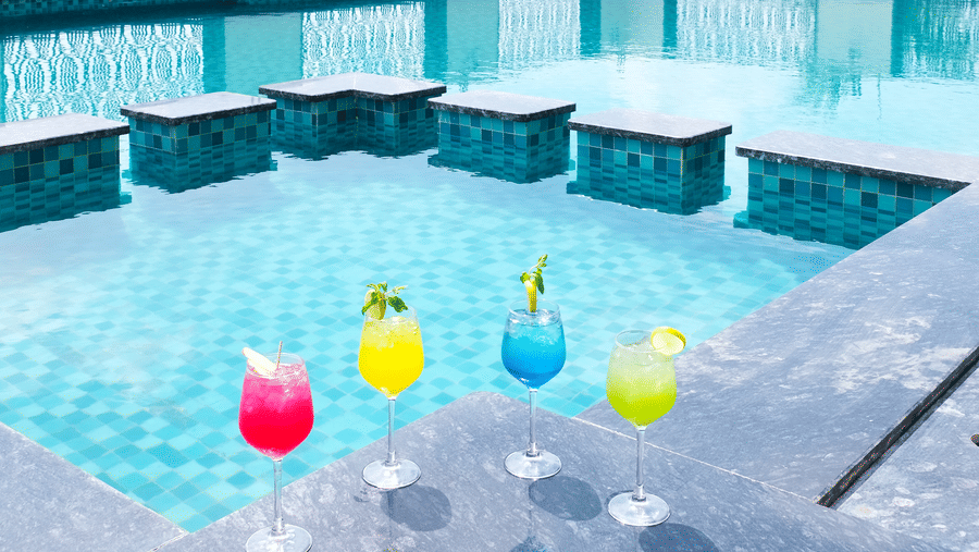 A swimming pool area with drinks lined up on a poolside table | Pride Premier Alwar