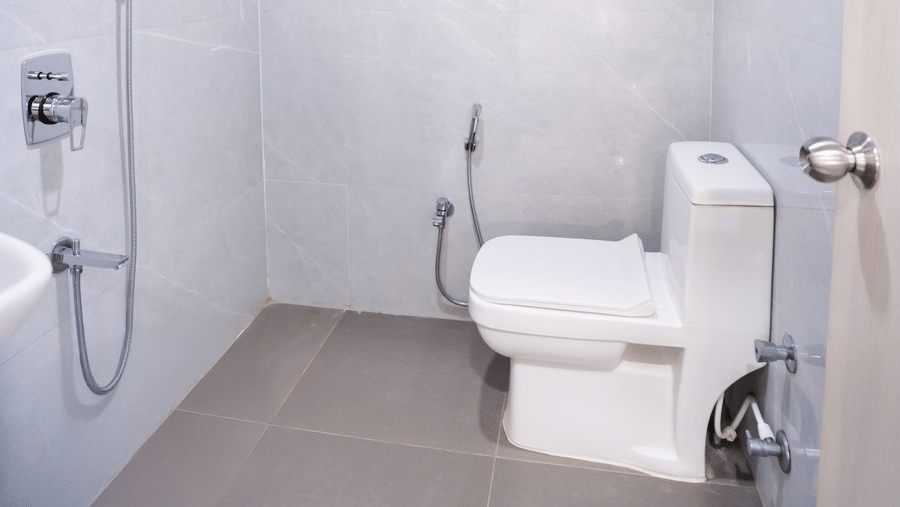 Spacious bathroom with a western toilet and shower area, brightly lit at Sunrise Business Hotel, Hyderabad.