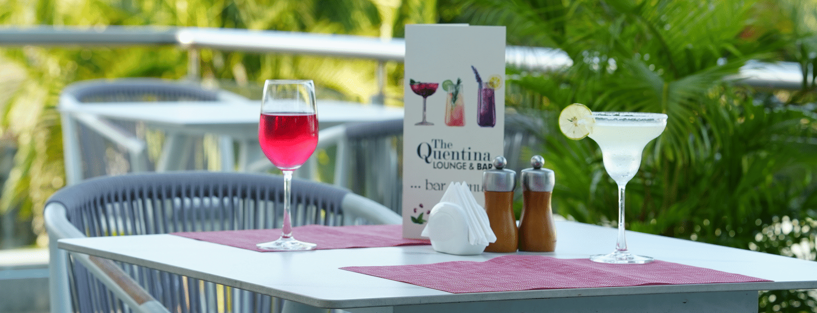 Outdoor table with chairs arranged beside plants and a menu card on the table at Grande Bay Resort & Spa.