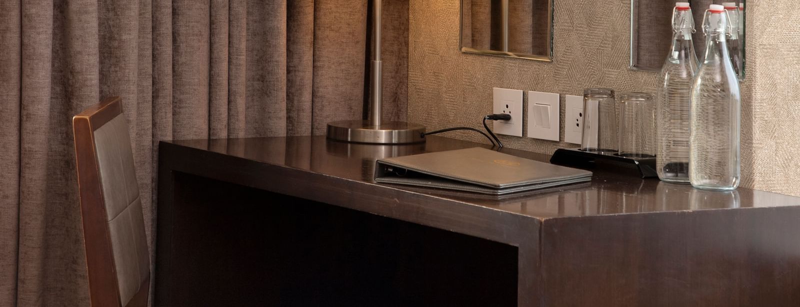 A workstation with water bottles, sockets, and a table lamp at The Hamuse Hotel, Kodaikanal