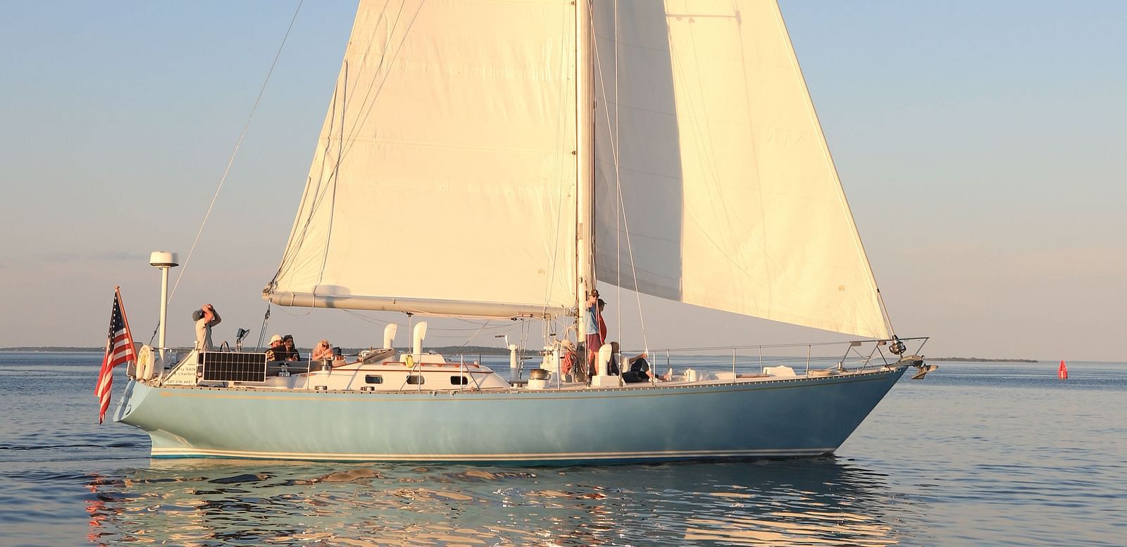 White sailboat gliding on calm waters at sunset near Hartstone Inn.