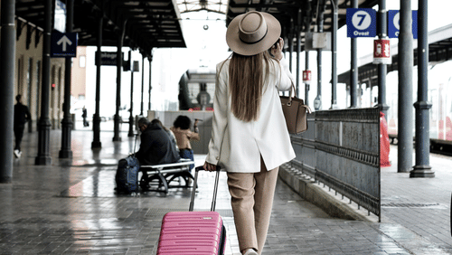Traveller pulling a suitcase while walking through a covered station walkway.