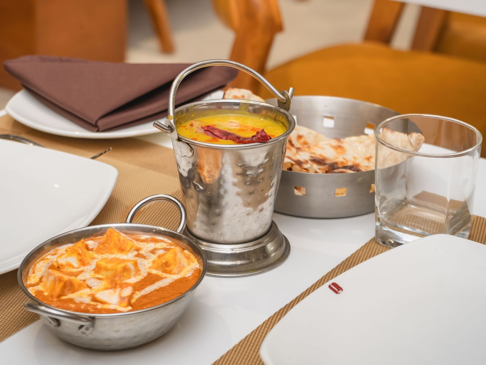 Bowls of food and drinks are arranged on a set table in a restaurant with empty chairs - Lords Eco Inn Ambaji.