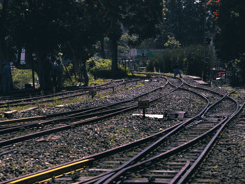 Railway tracks curve through lush greenery beneath a bright sky in the Nilgiri hills.