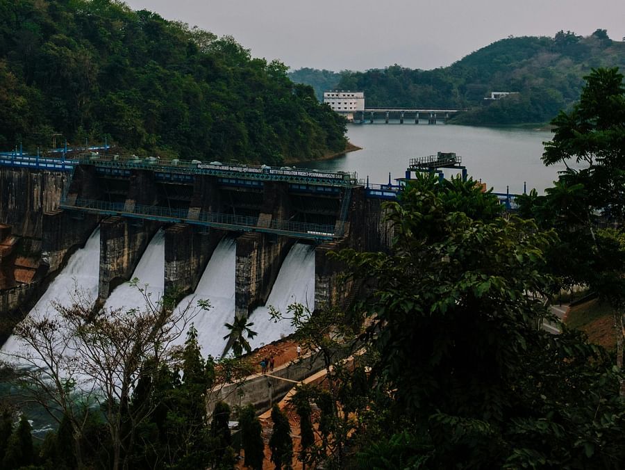 A wide shot of Ram Ganga Dam with water flowing over its spillway, surrounded by lush green hills.
