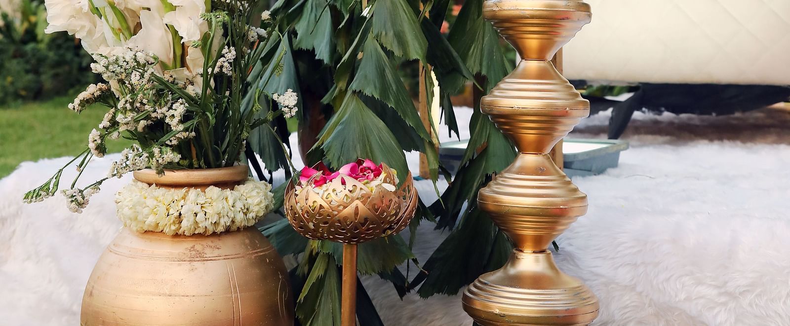 Tall brass lamp and large brass pots placed beside a bamboo and floral decor at Tisya Farms, Gurgaon.
