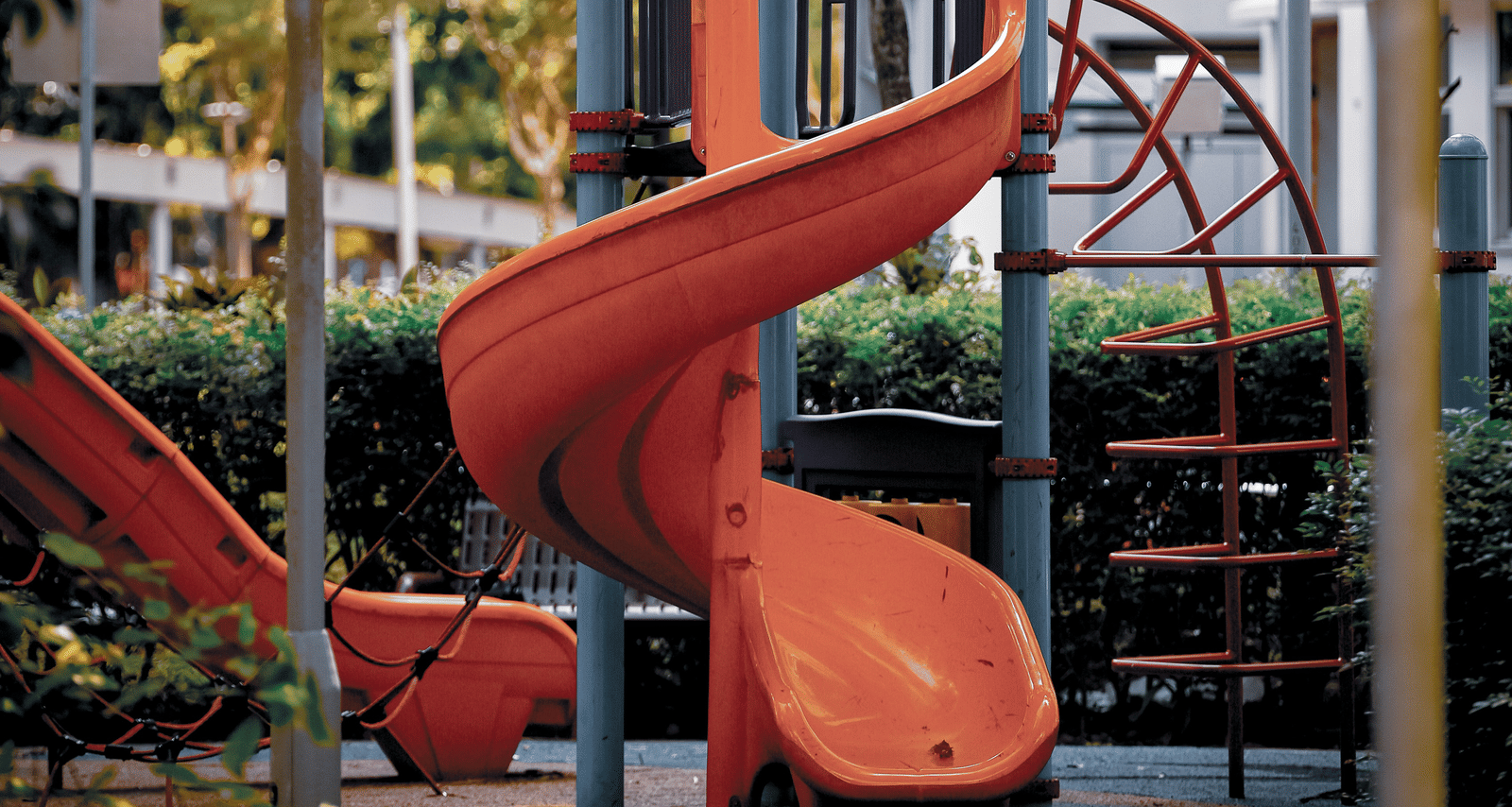 A small children's playground structure with two orange slides surrounded by greenery.